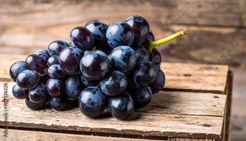 Clusters of ripe, dark purple grapes spill from their stem, nestled on a rustic wooden surface, evoking a sense of autumnal harvest abundance. photo