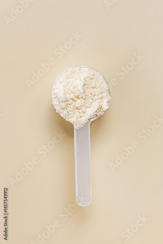 Plastic scoop filled with protein powder, placed on a plain beige surface,