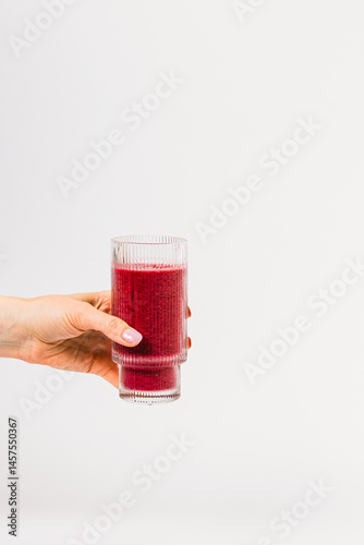 A hand holds a glass filled with a vibrant berry smoothie