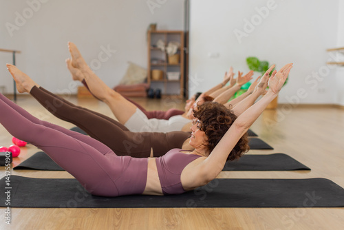 Obraz na płótnie Energetic core training moment with women in synchronized hollow body position on mats in barre pilates fusion workout