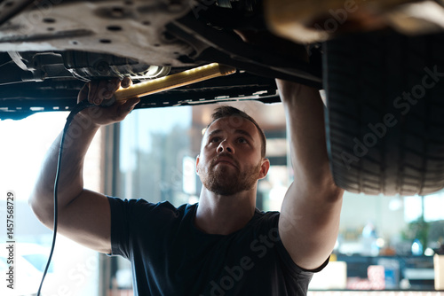 Obraz na płótnie Light, inspection and mechanic with car in workshop for service, maintenance or repair for safety. Torch, auto engineering and male industrial worker checking bottom of vehicle for oil leak in garage w salonie