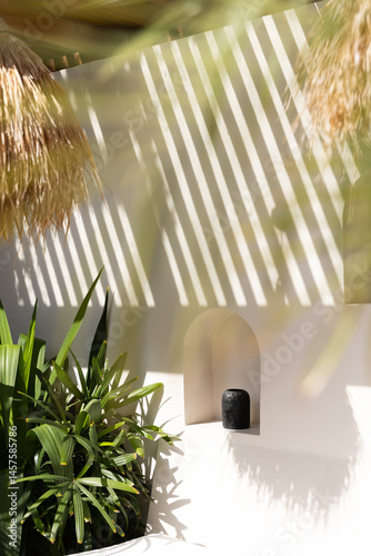 Vignette of decorated nook of a luxury villa in Bali with afternoon light shadows, leafy plants, sculptural ceramics, and straw lamps. 