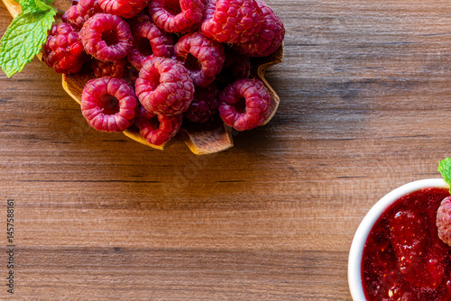Spoon with raspberry and bowl with raspberry jam on wooden background