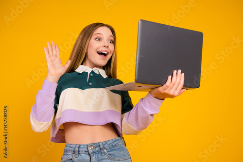 Young woman gesturing happily while holding a laptop against yellow background
