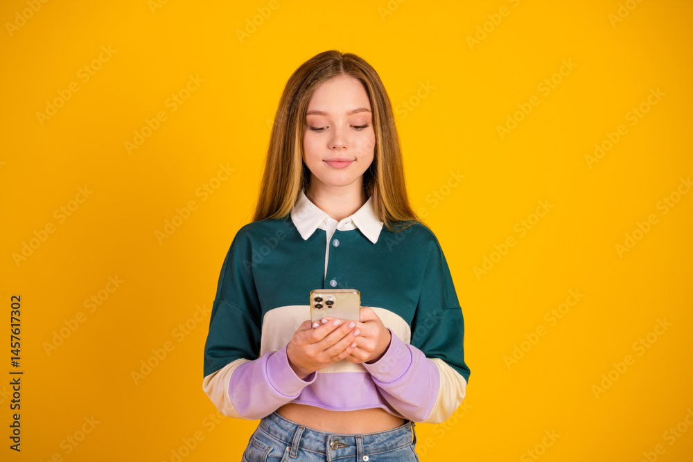 Lovely woman using smartphone in casual outfit against vibrant yellow background, showcasing modern lifestyle