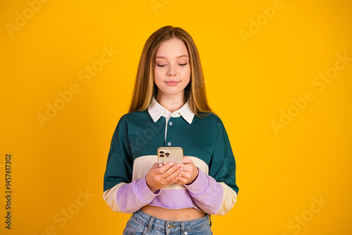 Obraz na płótnie Lovely woman using smartphone in casual outfit against vibrant yellow background, showcasing modern lifestyle w salonie