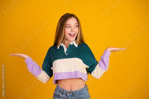 Obraz na płótnie Smiling young woman in casual pullover gesturing happily with hands amidst vibrant yellow background w salonie