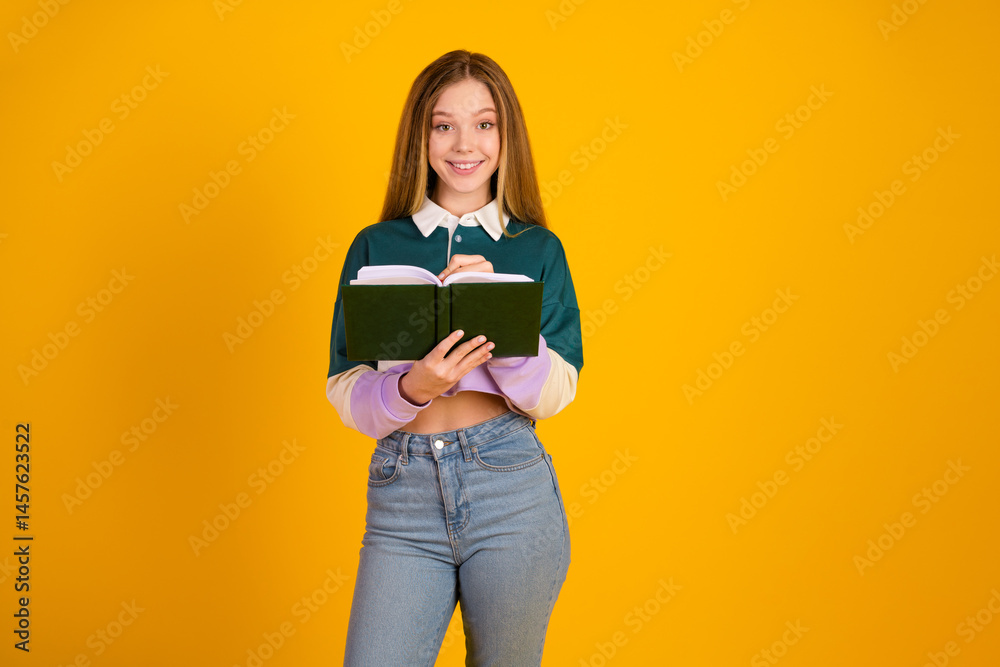 Cheerful young female in casual fashion holding a book on a yellow backdrop, embodying youth and educational pursuits
