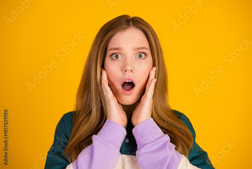 Obraz na płótnie Surprised young woman posing against a vibrant yellow backdrop, expressing shock with her hands on her face w salonie