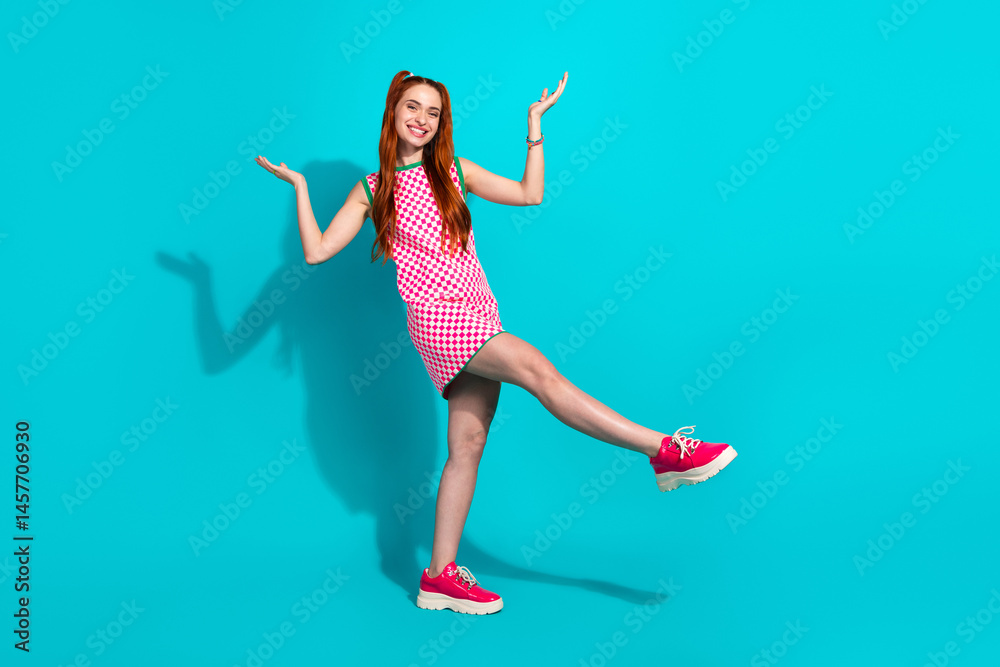 Naklejka premium Vibrant young woman posing in checkered summer dress against teal background, showcasing playful gestures and stylish fashion