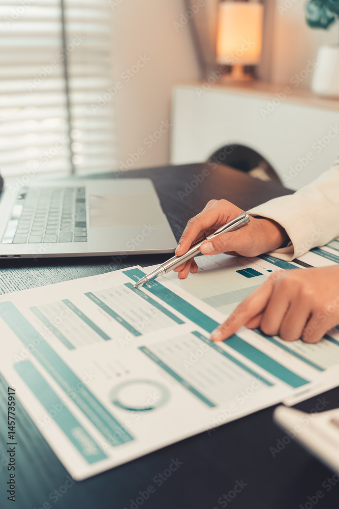 Young female accountant hand holding business investment analysis pen. Accounting, finance expert working with financial data and calculations with graph paper document. Vertical close up.