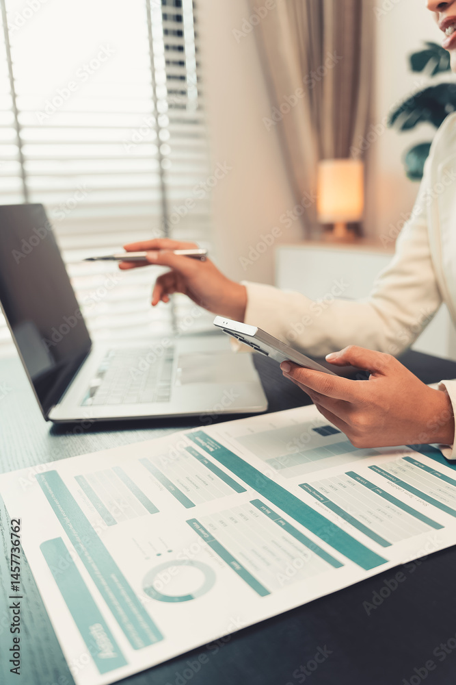Young female accountant hand holding business investment analysis pen. Accounting, finance expert working with financial data and calculations with graph paper document. Vertical close up.