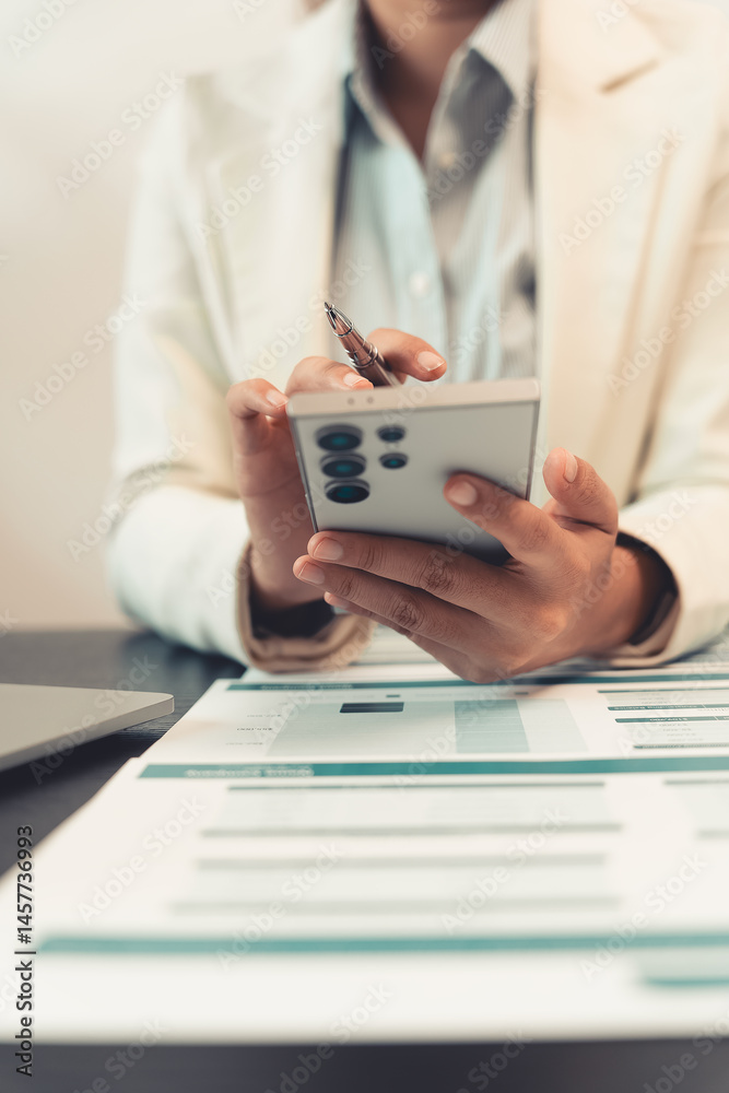 Young female accountant hand holding business investment analysis pen. Accounting, finance expert working with financial data and calculations with graph paper document. Vertical close up.