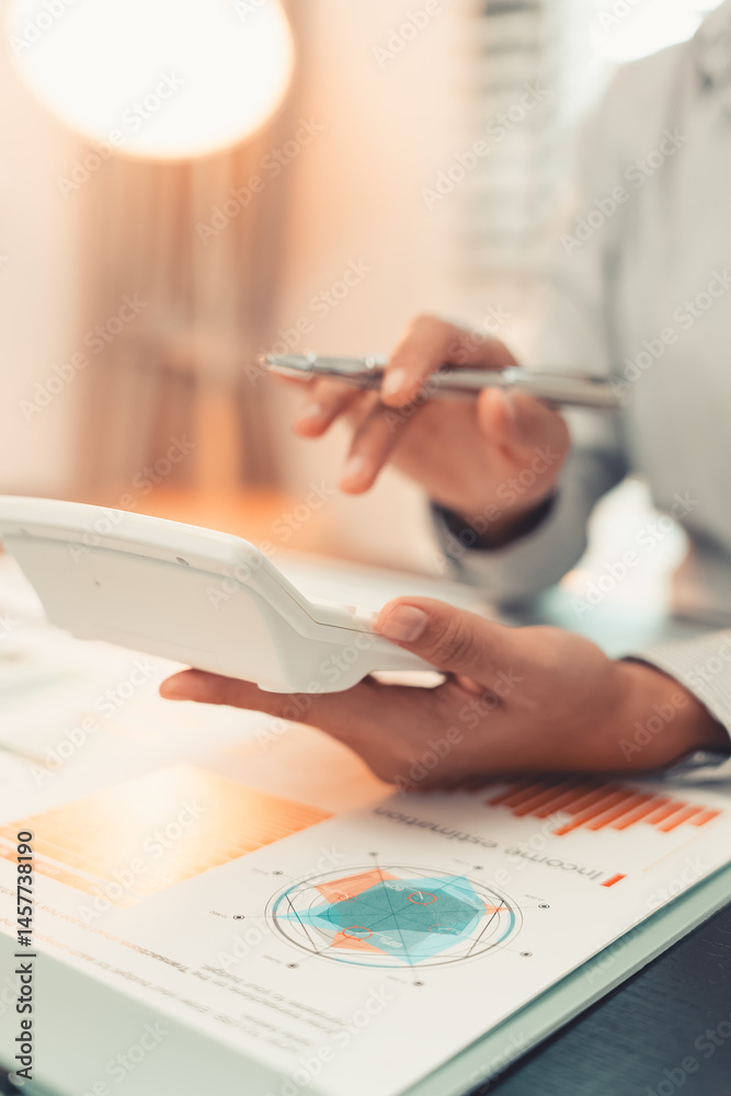 Young female accountant hand holding business investment analysis pen. Accounting, finance expert working with financial data and calculations with graph paper document. Vertical close up.