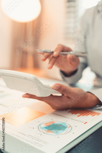 Obraz na płótnie Young female accountant hand holding business investment analysis pen. Accounting, finance expert working with financial data and calculations with graph paper document. Vertical close up. w salonie
