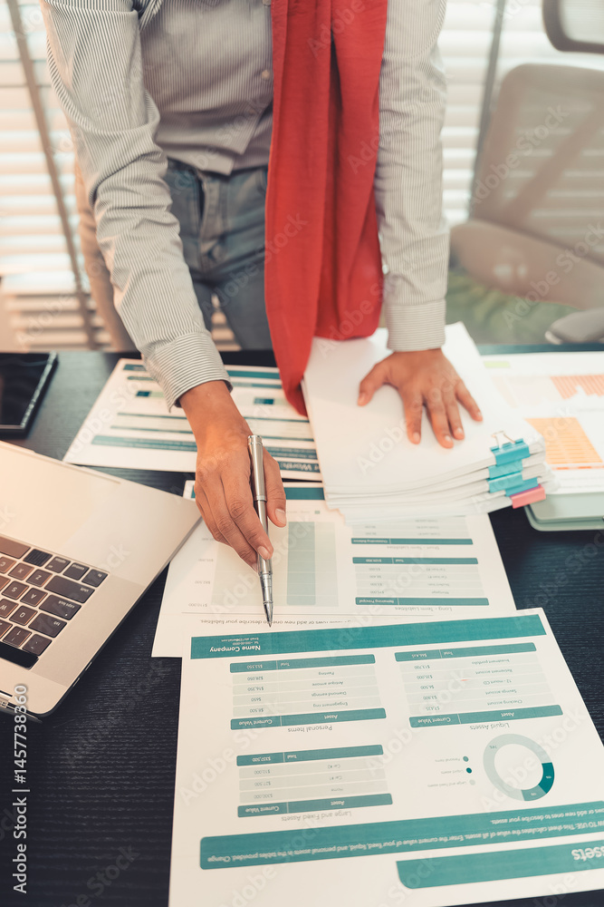 Young female accountant hand holding business investment analysis pen. Accounting, finance expert working with financial data and calculations with graph paper document. Vertical close up.