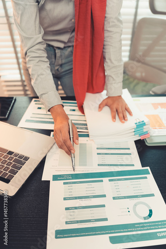 Young female accountant hand holding business investment analysis pen. Accounting, finance expert working with financial data and calculations with graph paper document. Vertical close up.