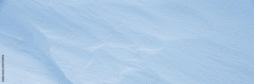 Fototapeta premium Beautiful winter background with snowy ground. Natural snow texture. Wind sculpted patterns on snow surface. Wide panoramic texture for background and design. Closeup top view with copy space.