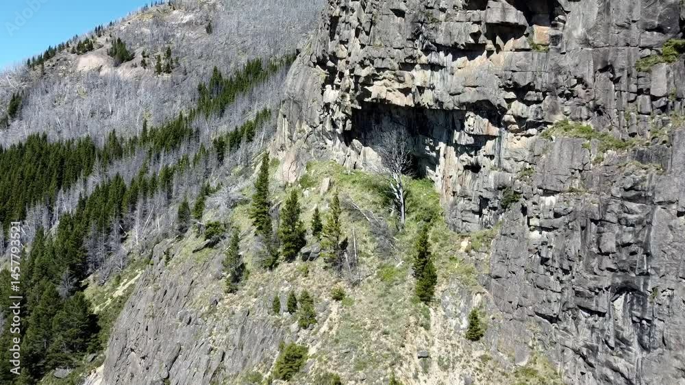 Vista aérea de una montaña en la Patagonia chilena, con laderas rocosas, bosque, una cueva y cielo despejado. El paisaje muestra la majestuosidad natural de la Región de Aysén en verano.