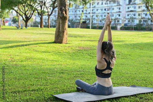Obraz na płótnie A woman is doing yoga in a park. The park is surrounded by buildings in the background. The woman is wearing a black top and gray pants. w salonie