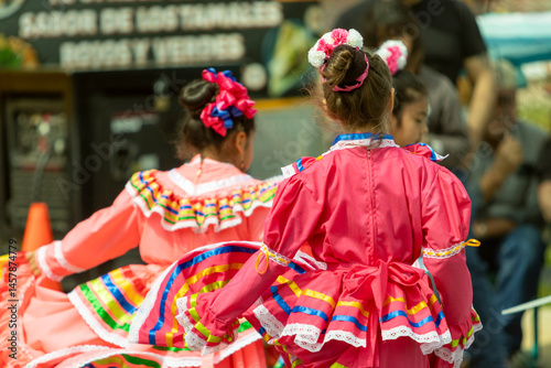 Little girls and other kids wearing traditional Mexican outfits during a cultural dance performance for Cinco de Mayo.