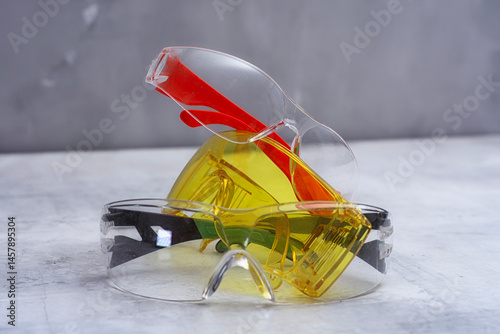 Set of protective safety glasses on a marble surface. Bright yellow lenses and clear lenses with red and green details. Concept for safety eye protection gear, and personal protective equipment.