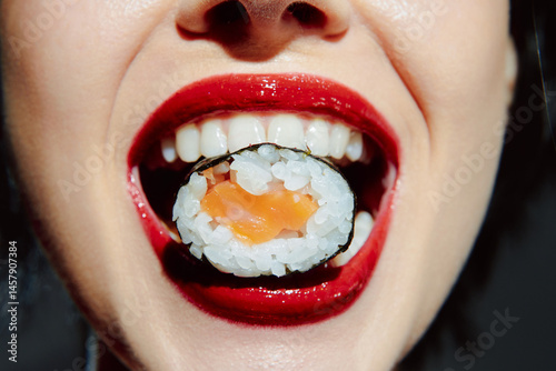 Obraz na płótnie Close-up of a woman enjoying sushi with a vibrant smile, showcasing dark hair, bold red lipstick, and a playful expression, against a soft background. w salonie
