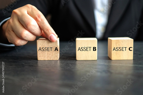 Hand Selecting 'ASSET A' from Three Wooden Blocks