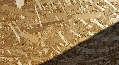 Close-up view of the rough texture and pattern of Oriented Strand Board (OSB) wood paneling with a diagonal shadow cast across the surface