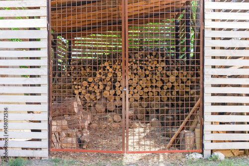 Stacked Firewood Behind Metal Gate in Woodshed photo