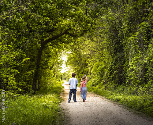 Young couple walking on trail in woody area in spring and taking selfie with phone; trees on sides form natural arch