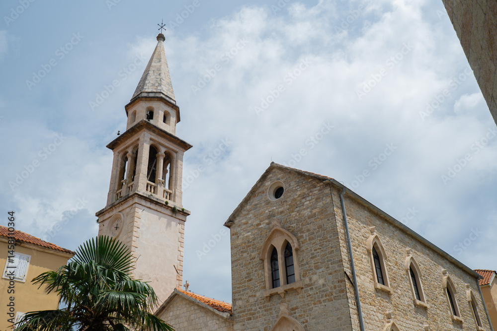 Fototapeta premium Budva, Montenegro picturesque old town and fortress walls architecture. Stunning showcasing historic stone buildings with red-tiled roofs traditional house. Spire of the chapel of The Church of Sveti