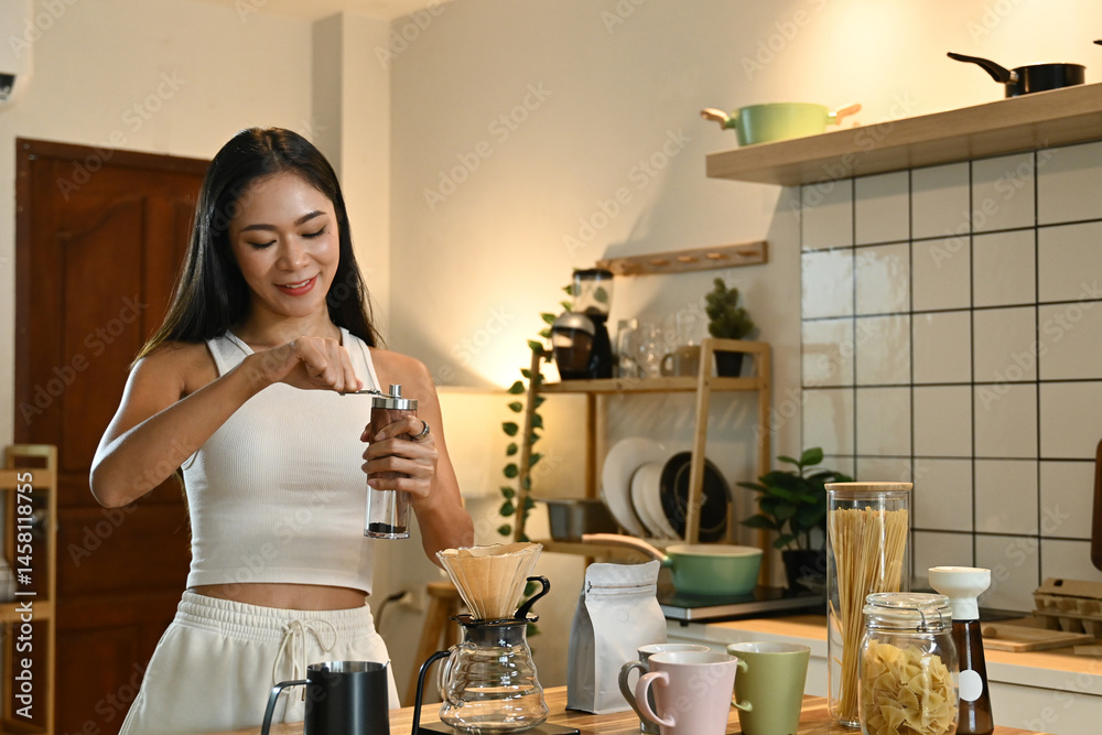 A woman is grinding coffee beans in a coffee grinder. The kitchen is well-equipped with various items.