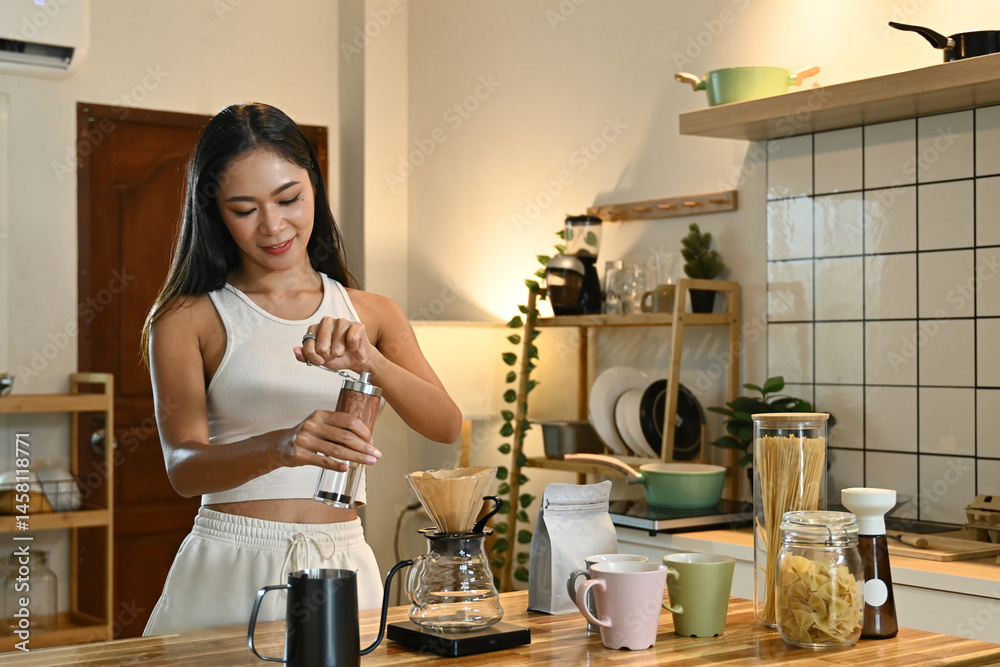 A woman is grinding coffee beans in a coffee grinder. The kitchen is well-equipped with various items.