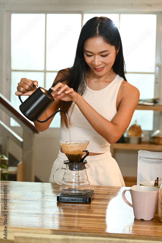 A woman is making coffee. She is smiling as she pours the coffee into a cup.