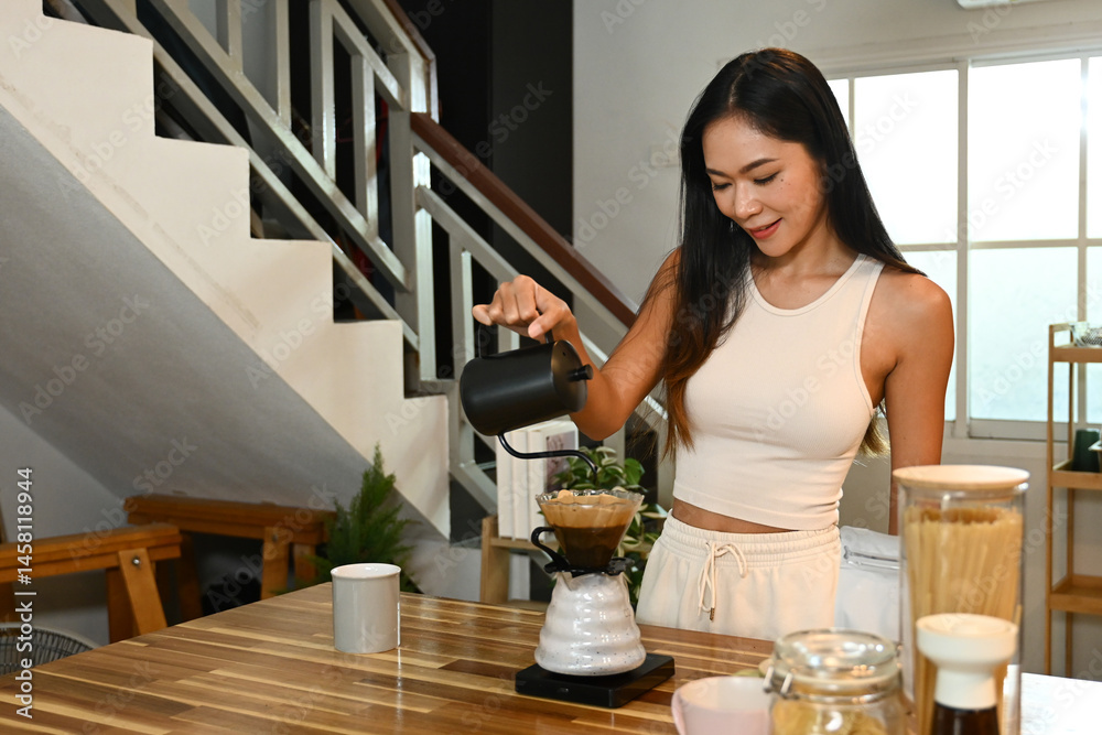 A woman is making coffee. She is smiling as she pours the coffee into a cup.