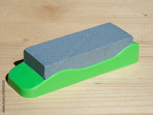 Sharpening stone with plastic base. Sharpening knives, scissors and chisels. Diamond grinding stone. Single grindstone or whetstone sharpener on wooden table