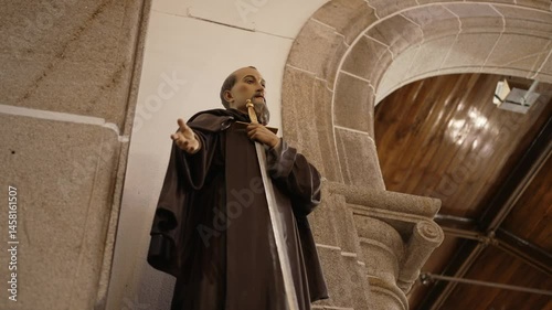 Religious statue of a monk with a cross inside a church beside an arched stone structure