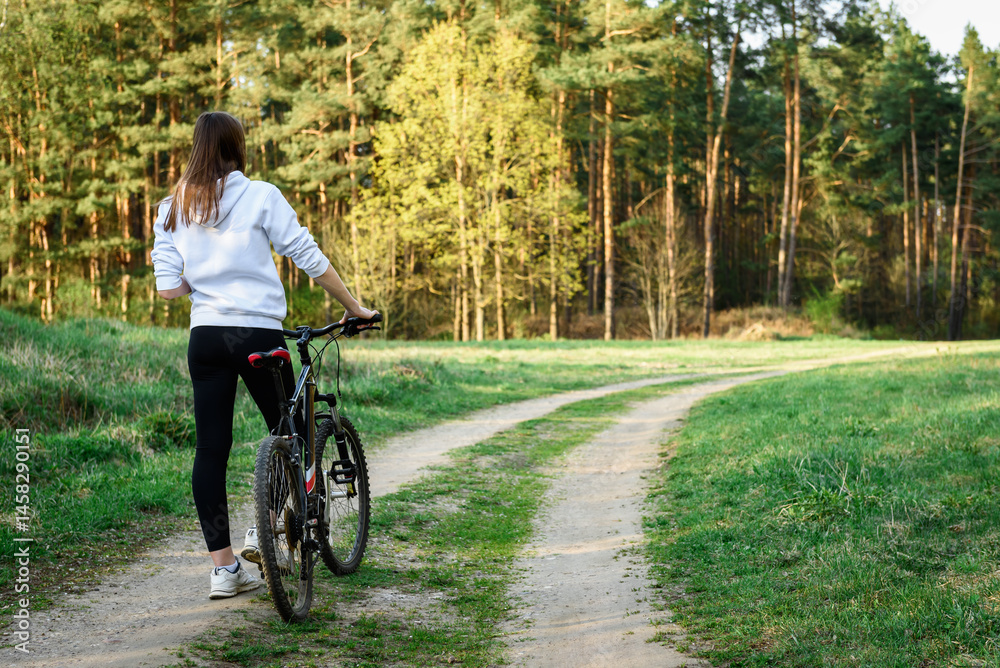 Obraz premium Female cyclist holding the handlebars of a mountain bike is going to ride outdoors against the background of a spring forest.