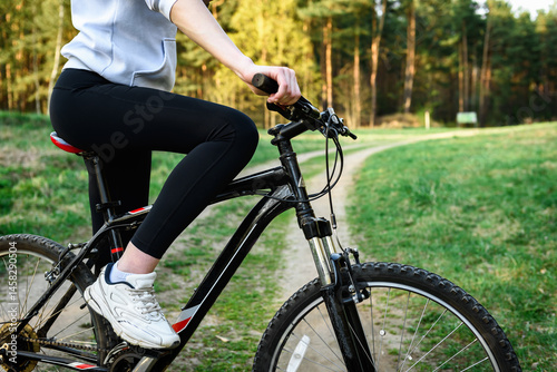 Woman cyclist holding handlebars of mountain bike outdoors on spring forest background.