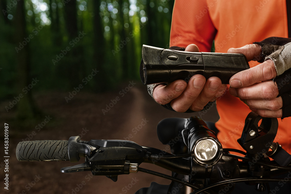 Obraz premium Closeup photo of athletic man holding taser to protect against stray animals during forest ride. Man riding bike with stun gun ready for dog protection, safety during solo adventure