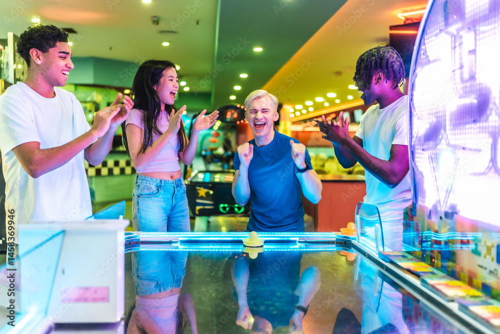 Excited friends clapping and playing air hockey in an amusement arcade