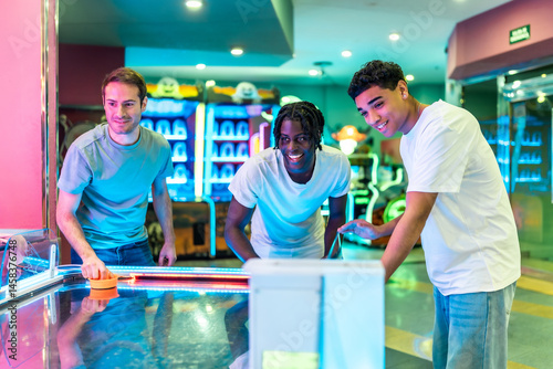 Multiethnic friends playing air hockey in entertainment center
