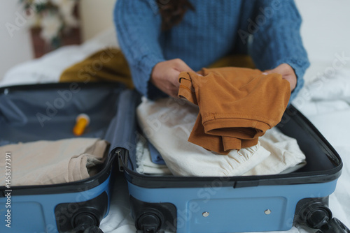 Woman carefully placing clothing items into an open suitcase on a bed, preparing for a trip or vacation, showcasing travel and organization concepts