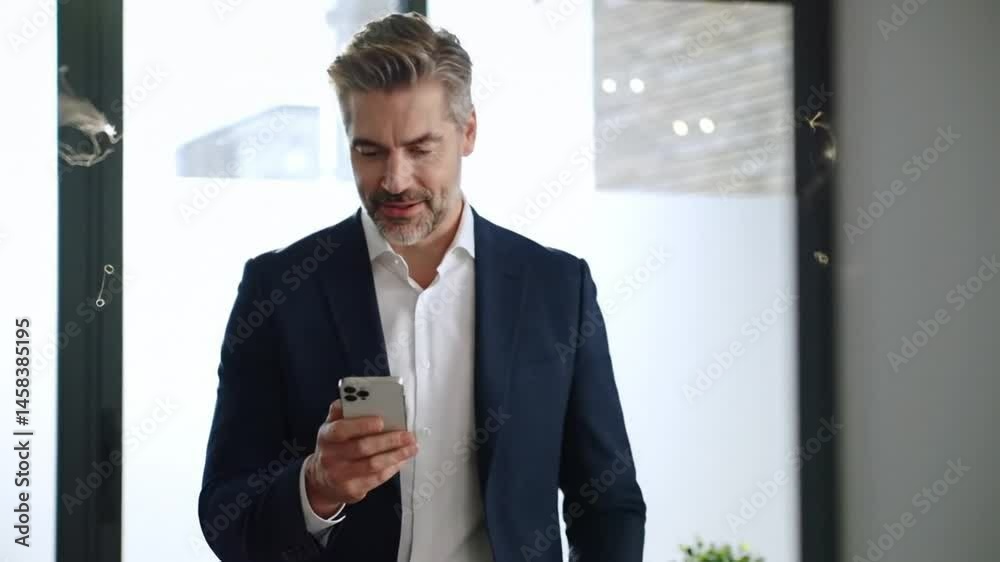 Happy confident mid aged male company ceo executive holding cellphone standing in office using business mobile apps Happy confident mid aged male company ceo executive holding cellphone standing in office using business mobile apps