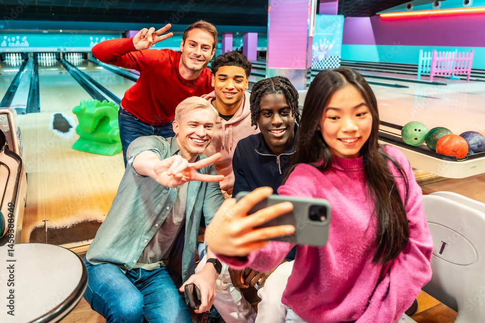 Happy multi ethnic friends taking selfie and gesturing peace sign at bowling alley