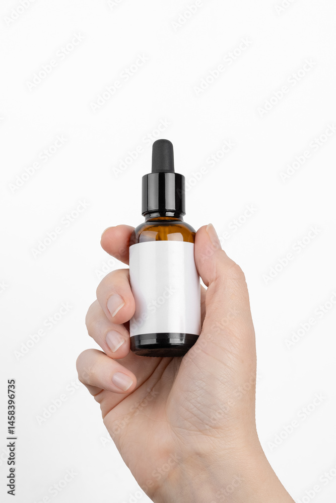 Naklejka premium Mockup of a glass bottle with a dropper. In a woman's hand. Cosmetics hair oil. Empty label. Place for an inscription and logo.
