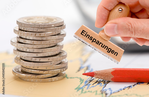 Ein Holzstempel ist beschriftet mit Einsparungen über einem Finanzchart mit Rotstift - FOTOMONTAGE