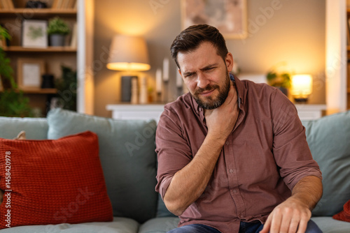 Tableau sur toile Man sitting on a sofa, holding his throat in discomfort, feeling a sore throat
