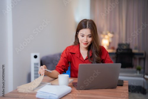 Konstfotografi Young Asian businesswoman wearing a vibrant red shirt smiles while working from